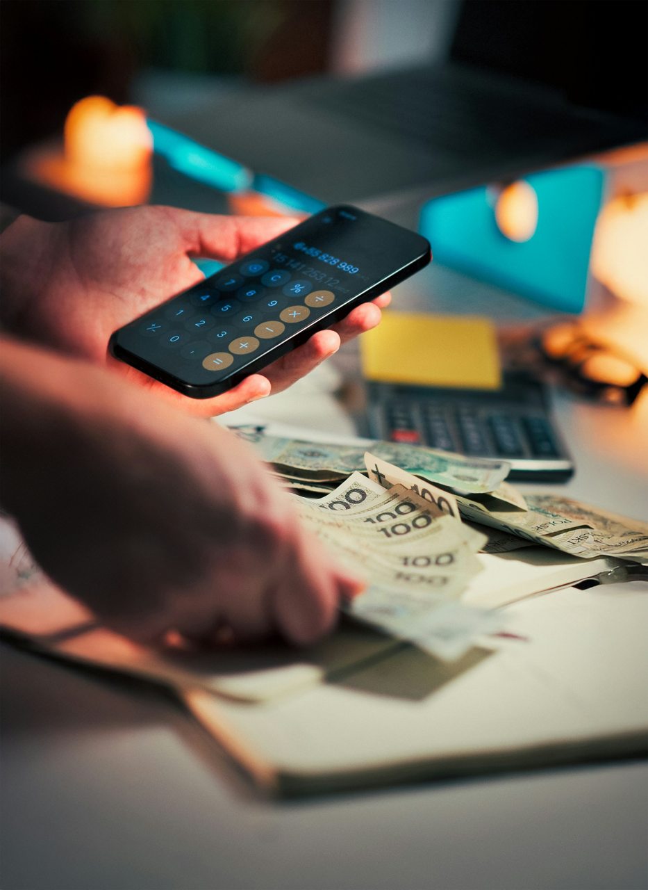 Hands counting banknotes beside a phone calculator