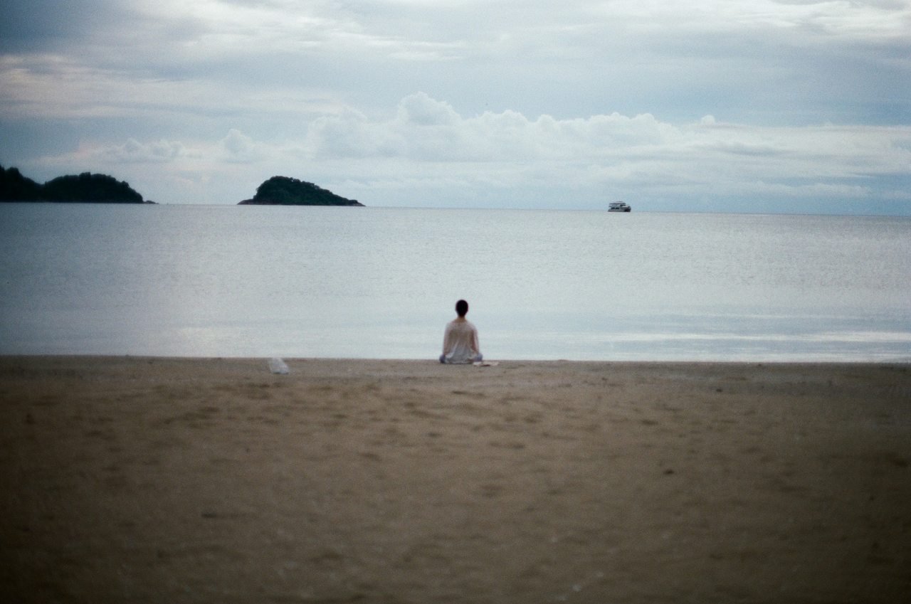 Person sitting on a quiet beach facing the ocean